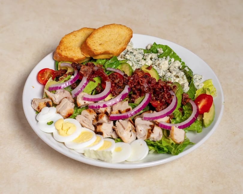 Cobb salad with grilled chicken, bacon, avocado, blue cheese, red onion, tomatoes, and hard-boiled eggs.