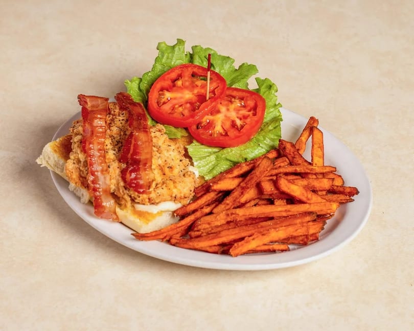 Chicken sandwich with bacon, lettuce, and tomato, served with a side of sweet potato fries.