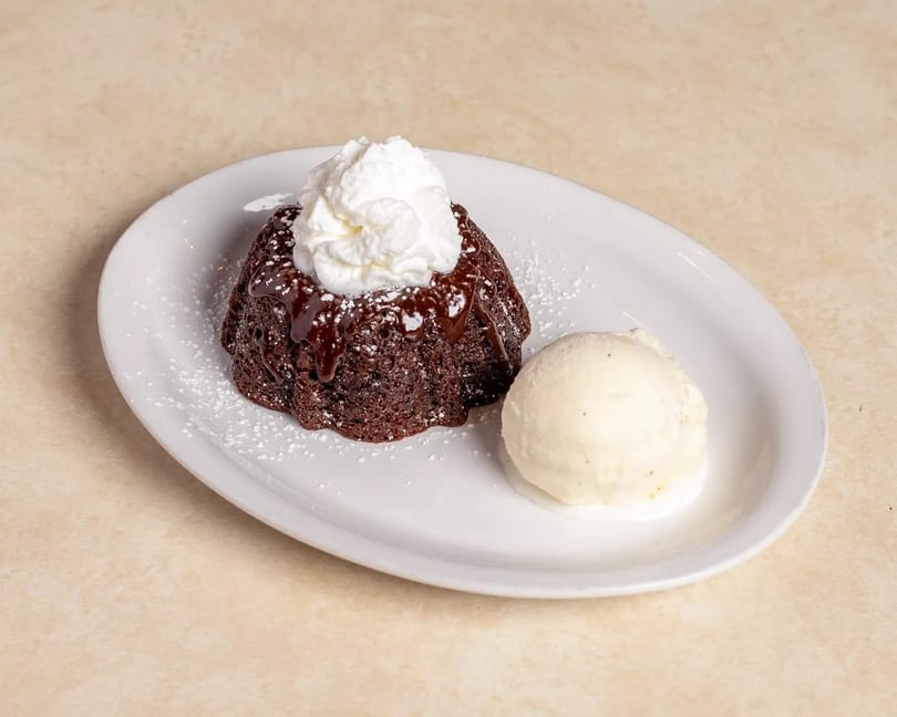 Chocolate lava cake with whipped cream, chocolate drizzle, powdered sugar, and a scoop of vanilla ice cream.